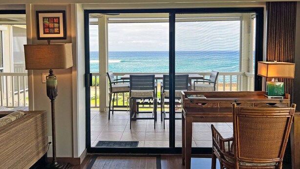 Une pièce avec vue sur l’océan, une table à manger avec des chaises, une lampe et un fauteuil en osier.