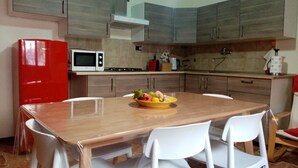 Una cucina con un tavolo di legno, sedie bianche, un frigorifero rosso, un forno a microonde e una cucina a gas.