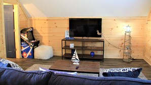 Una sala de estar acogedora con detalles de madera, un televisor de pantalla plana en la pared, un pequeño modelo de velero sobre una mesa de centro y una lámpara de pie.