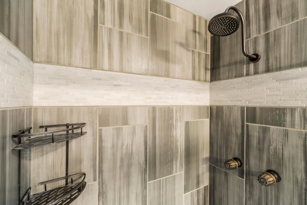 A shower area with a wooden panel design, a metal shelf, and a handheld showerhead.