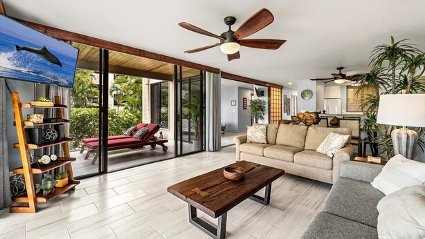 A spacious living room with a wooden coffee table, a sofa, and a television displaying a dolphin. - Keauhou Kona Surf & Racquet Club#6-101 (Kailua-Kona)