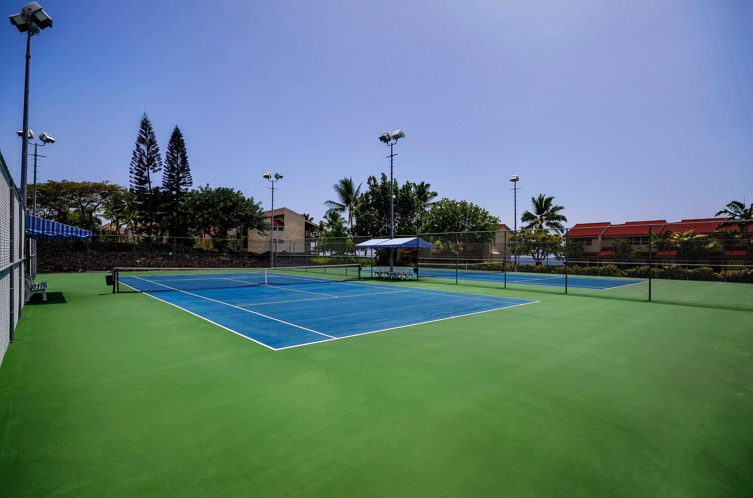 Canchas de tenis múltiples, rodeadas por una cerca y equipadas con iluminación artificial.