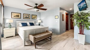A bedroom with a bed, bedside tables, a bench, a ceiling fan, framed pictures on the wall, and a potted plant. - Keauhou Kona Surf & Racquet Club#6-101 (Kailua-Kona)