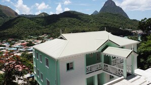 A two-story building with a green and white color scheme, a balcony, and a view of a mountainous landscape. - *Sugarmon Villas* Mout Gimmie Suite with amazingPergola Balcony View! (Soufriere)