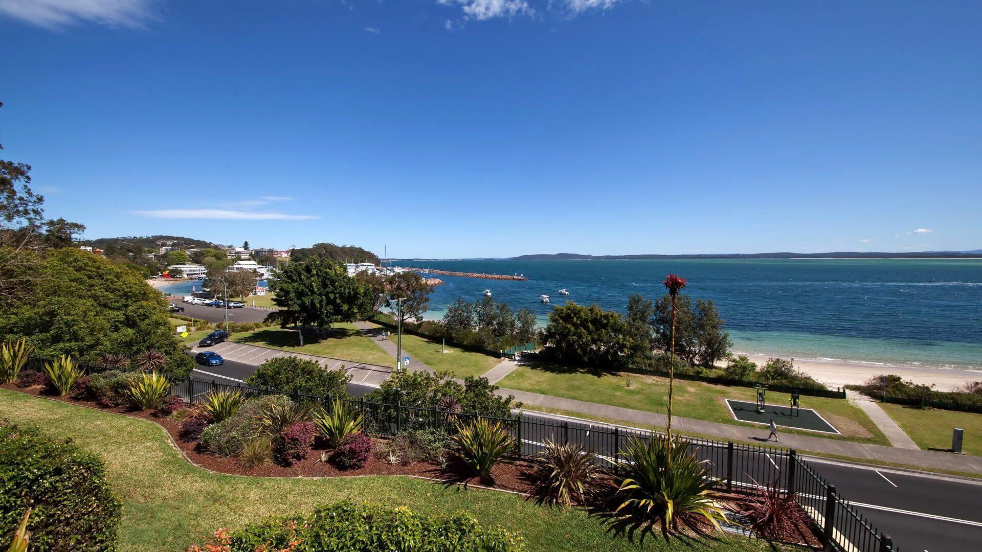 A coastal view with a road, parking area, and greenery.