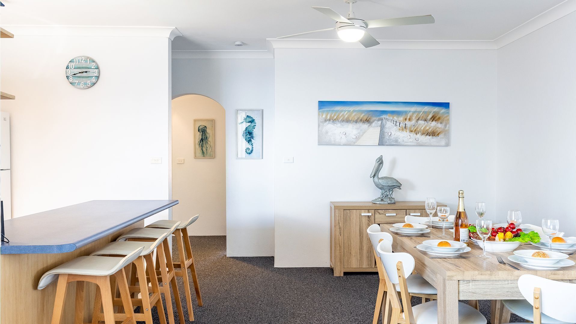 A dining area with a wooden table set for four, a ceiling fan, and artwork on the walls.