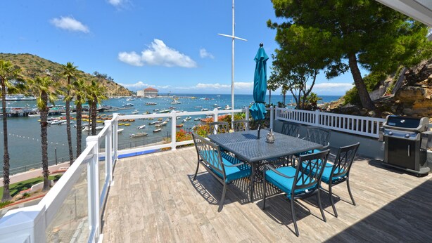 Eine Terrasse mit Tisch und Stühlen mit Blick auf einen Yachthafen, Boote und eine hügelige Landschaft.