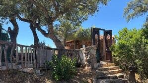 A rustic stone pathway leading to a wooden gate, surrounded by trees and a stone building.