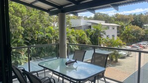 A balcony with glass tables and chairs, overlooking a parking area and a building with a white facade. - Baden 80 - Rainbow Shores. Air conditioned Unit - Top Floor - Walk To Beach (RAINBOW BEACH)