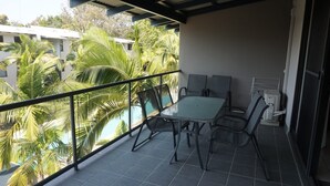 A balcony with a table and chairs, overlooking a pool and palm trees.