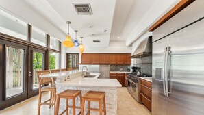 Une cuisine moderne dotée d’un grand îlot central, d’appareils électroménagers en acier inoxydable et de tabourets de bar en bois.