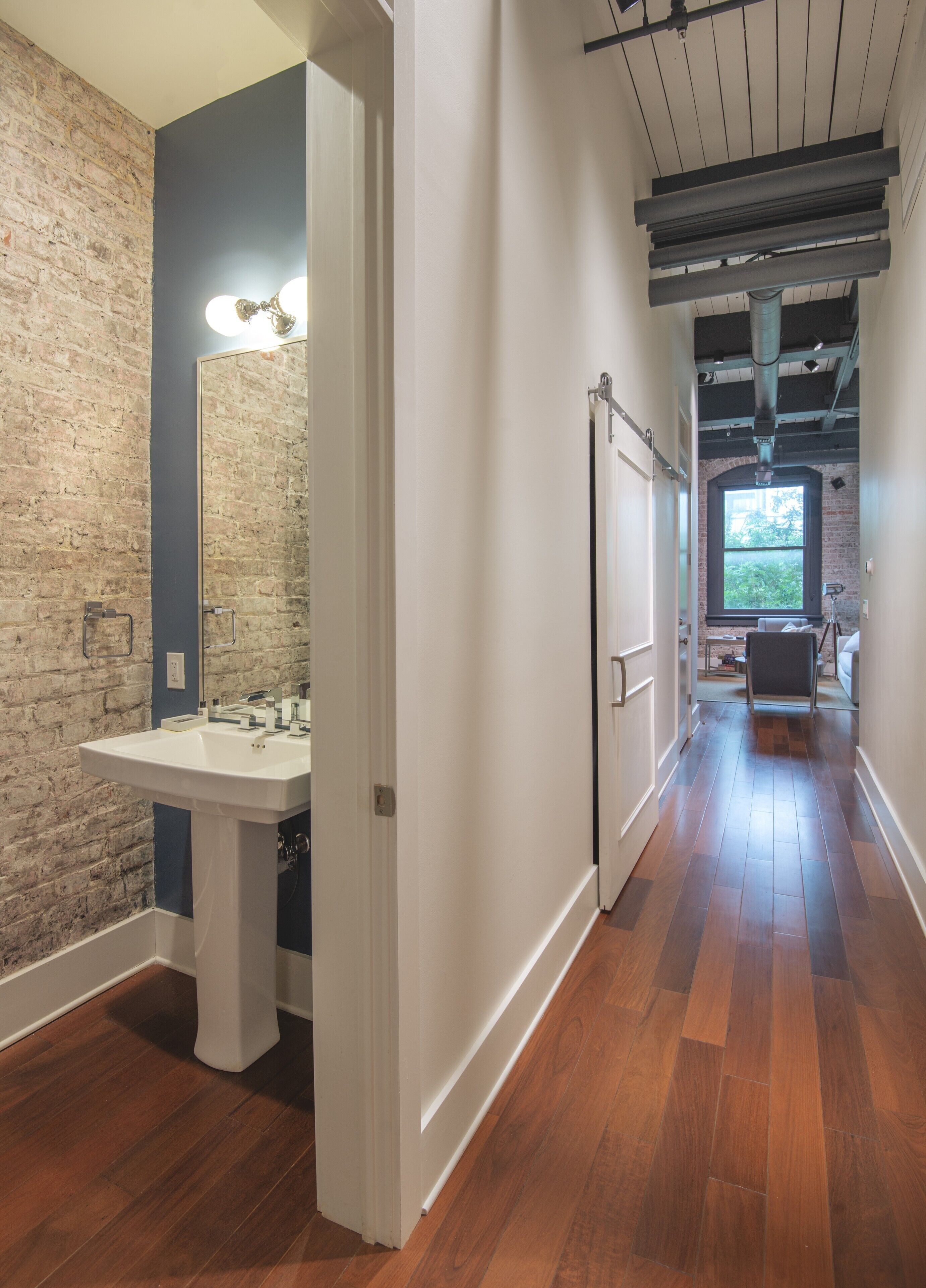 A hallway with a wooden floor, a white sink, and a brick wall.