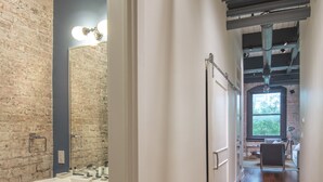 A hallway with a wooden floor, a white sink, and a brick wall.