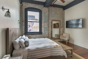 A bedroom with a bed, a TV, a chair, and a window with a view of buildings.