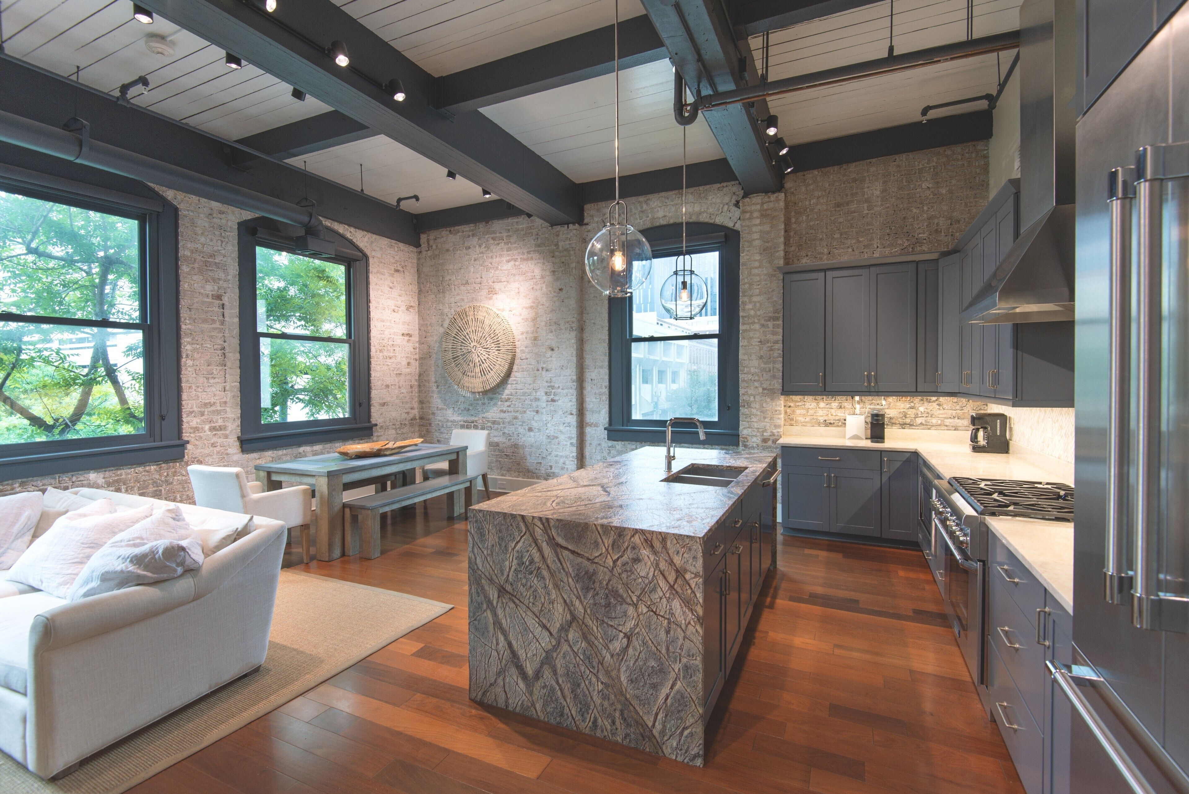 Una cocina moderna con una isla grande, armarios oscuros y vistas al exterior a través de amplios ventanales.