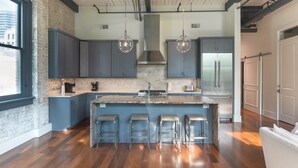 A modern kitchen with a large island, bar stools, and a stainless steel refrigerator.