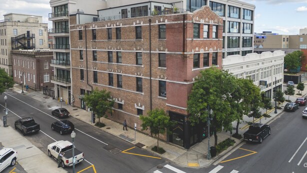 A multi-story building with a mix of brick and modern glass facades, located at a street corner with visible road markings and parked cars.