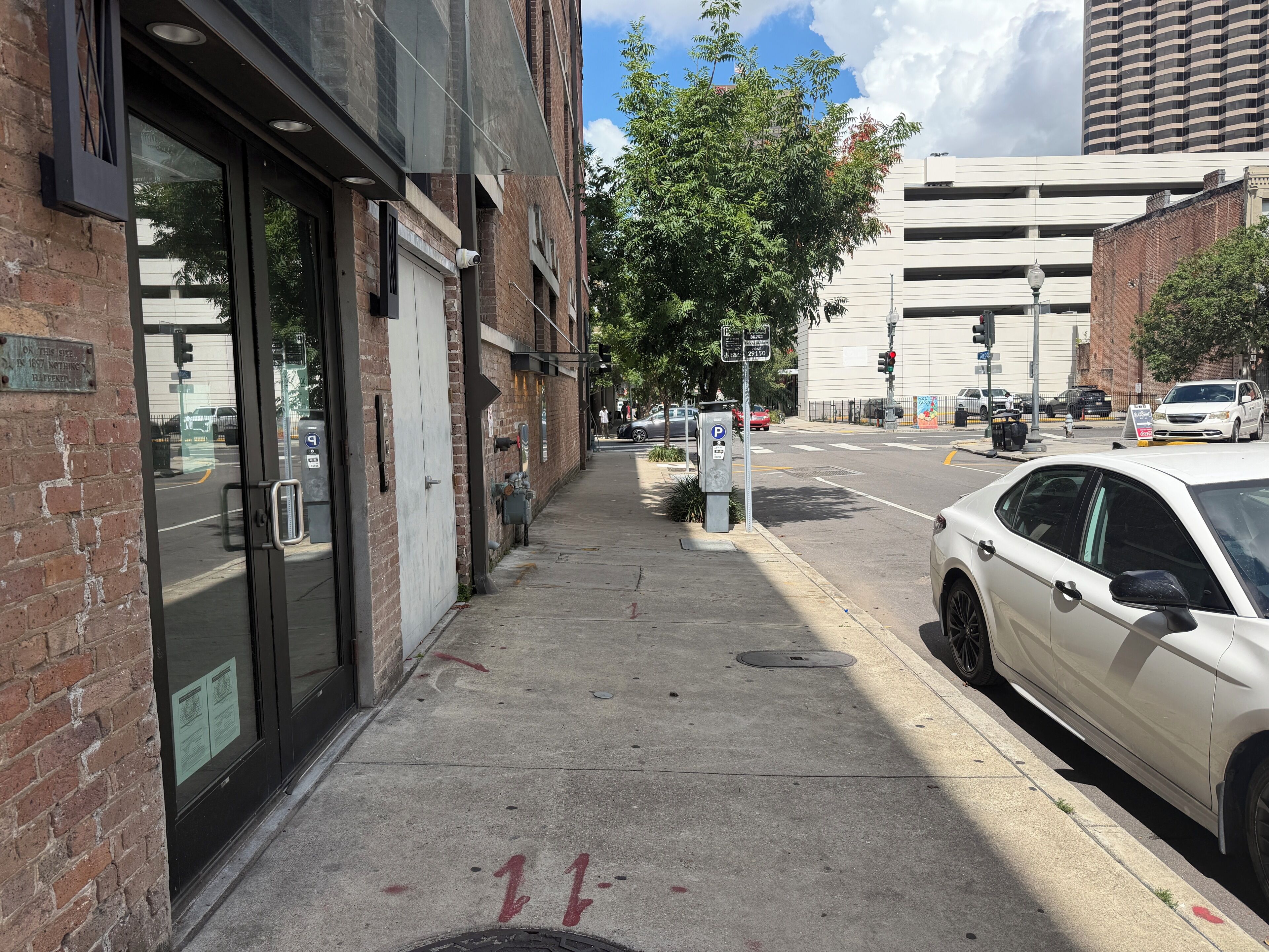 A street view with a building featuring a brick facade, a garage door, and a parking meter.
