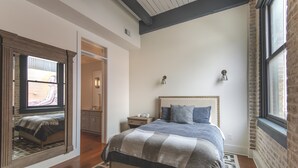 A bedroom with a large bed, a nightstand, a dresser, and a mirror.