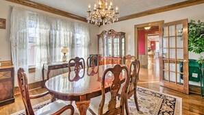 Comedor con mesa de madera, sillas, candelabro y un ventanal con cortinas.