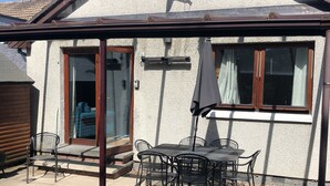 Ein Garten mit einer Terrasse, einem Tisch, Stühlen, einem Grill und einem Fenster mit Blick auf einen Garten.