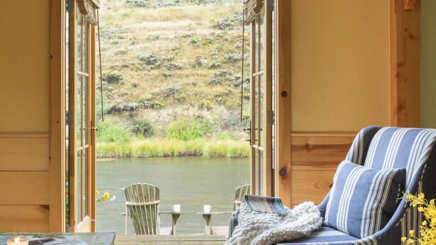 Una habitación acogedora con un ventanal grande, una mesa de madera con una vela, un sofá a rayas y vistas a un área verde.