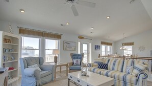 Un salon spacieux avec un canapé bleu, un canapé à rayures et une table basse en bois. On y trouve des étagères, un lustre et une vue sur l’extérieur.