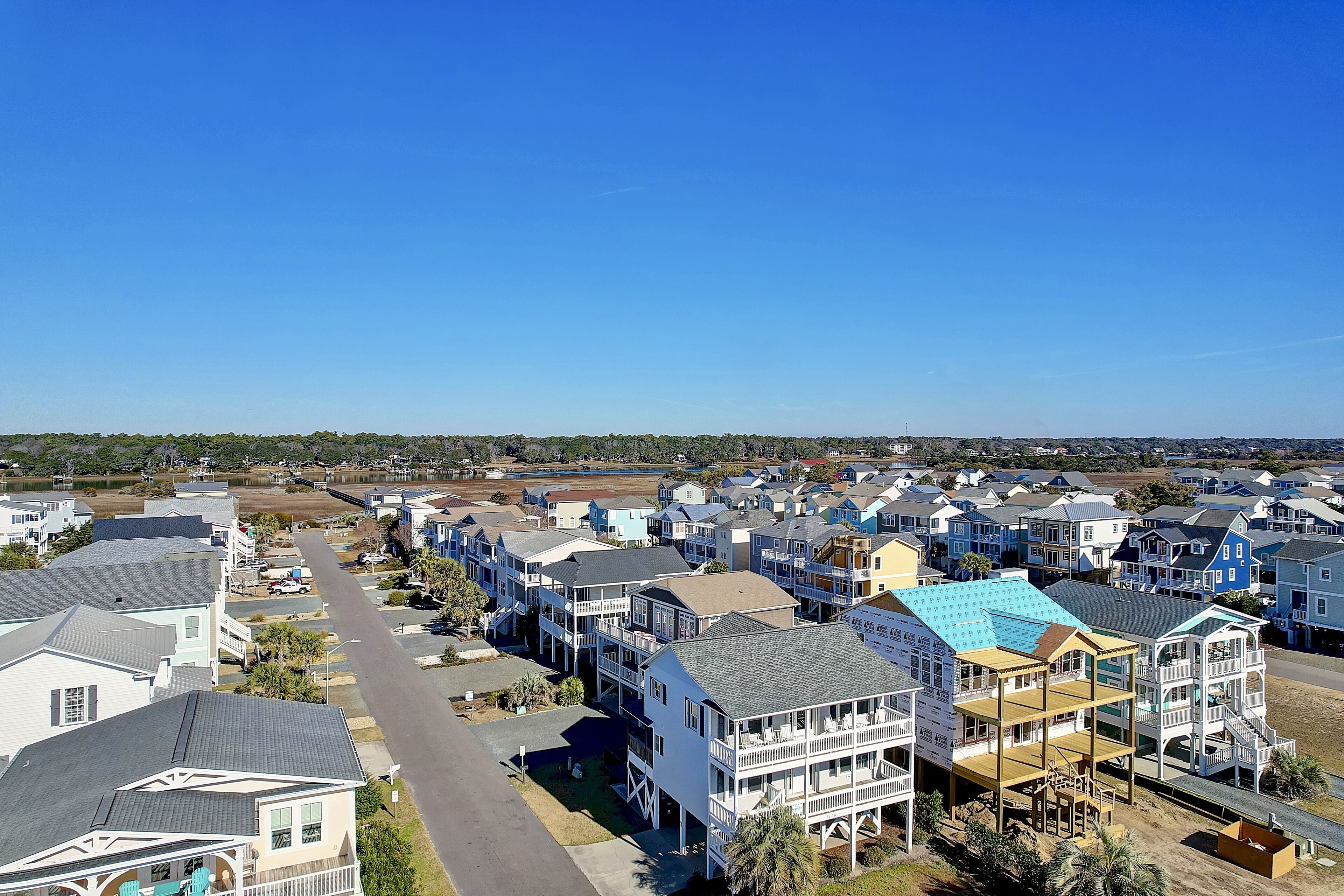 A coastal residential area with multi-story houses, a clear sky, and a beach in the background.