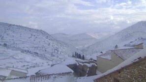 A snow-covered village with traditional stone buildings and a mountainous backdrop. - 1º-APT-CASA ANGELITA (Olocau Del Rey)