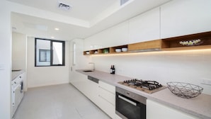 A modern kitchen with white cabinets, a built-in oven, a gas stove, and a window. - 405 PINE TREE | Short walk to beach | Accom Holidays (TERRIGAL)