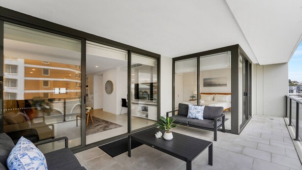A modern apartment with a balcony, a dining area, and a living room with a sofa and a coffee table. - 405 PINE TREE | Short walk to beach | Accom Holidays (TERRIGAL)