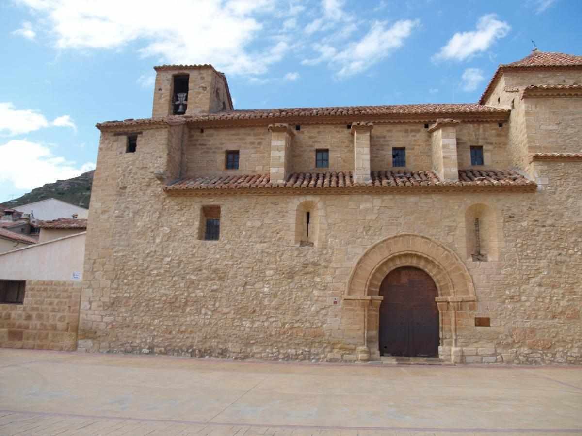 Un edificio de piedra con tejado de tejas, una entrada central en arco y un campanario.