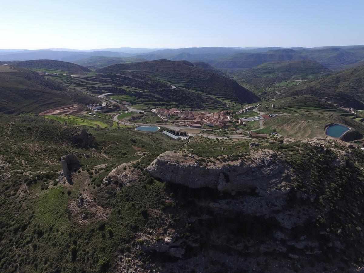 A mountainous landscape with terraced fields, a small settlement, and a large rock formation.