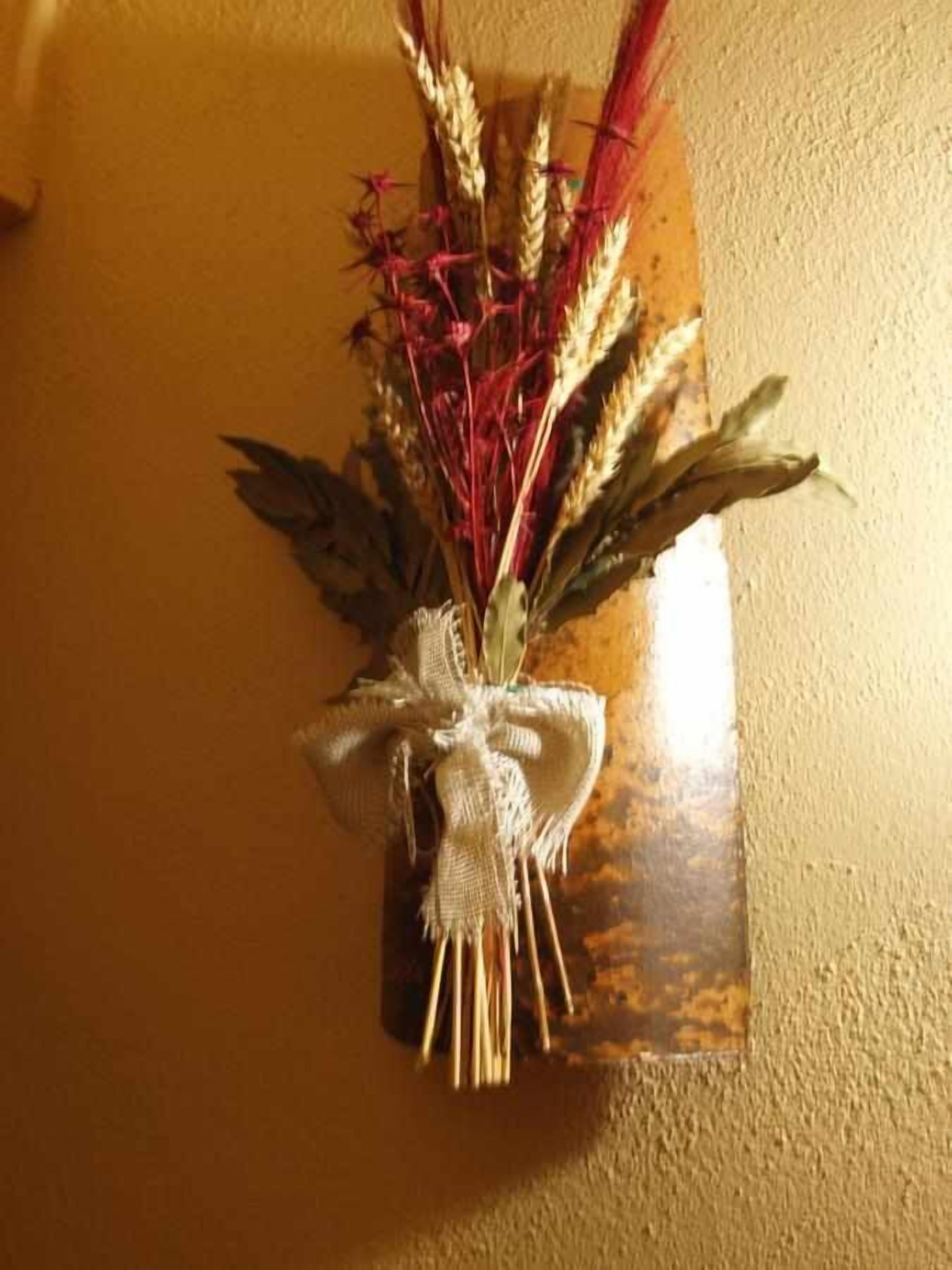 Decoración rústica montada en la pared con plantas secas y un lazo de arpillera.