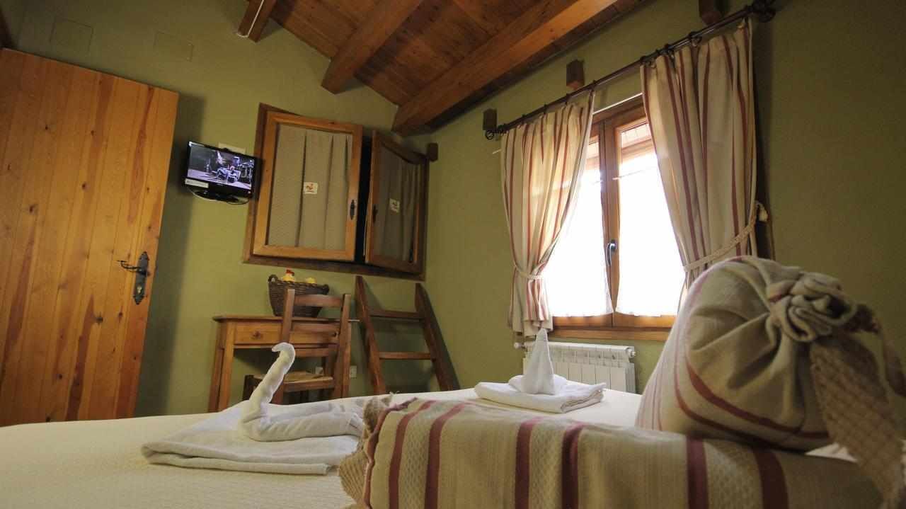 Une chambre avec un lit, une armoire en bois, un téléviseur fixé au mur et une fenêtre avec des rideaux.