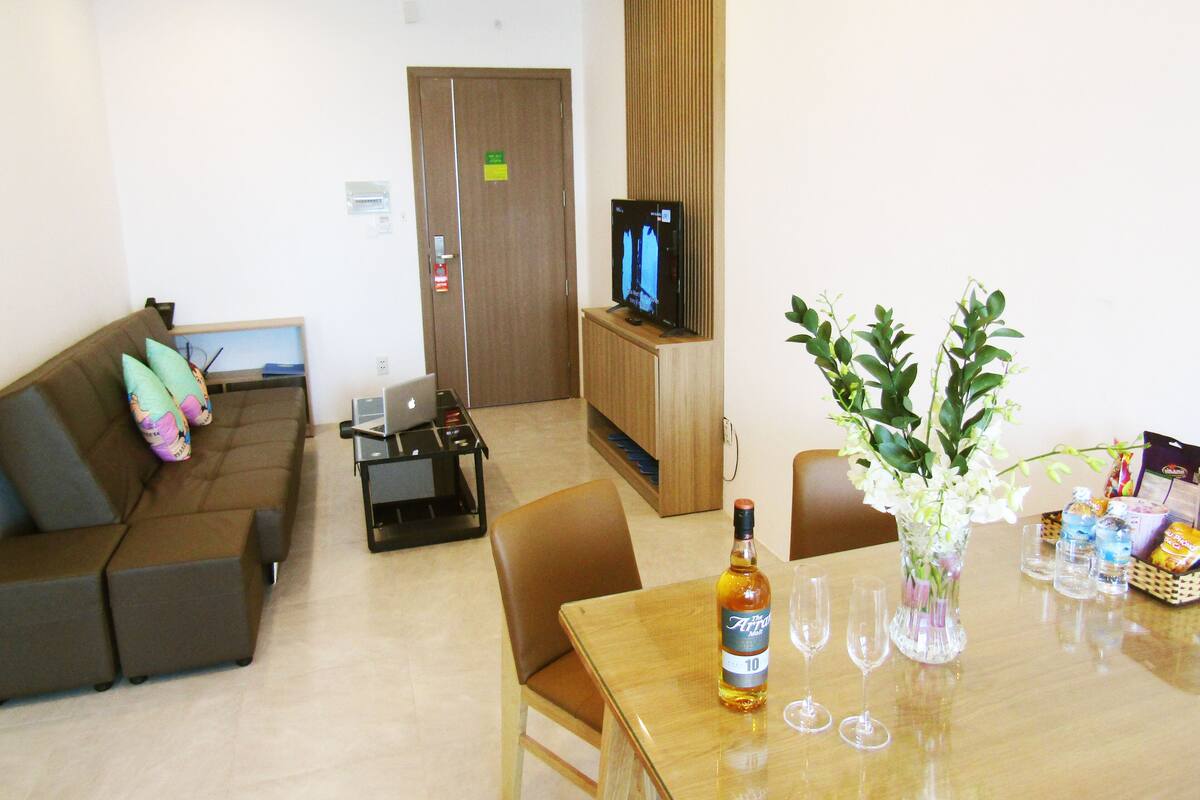 A living room with a sofa, a dining table with a bottle and glasses, a TV, and a plant.