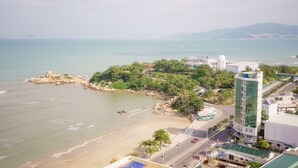 A coastal hotel with a beach view, a parking area, and a road with vehicles. - SoHo Apartment (Bac Nha Trang)
