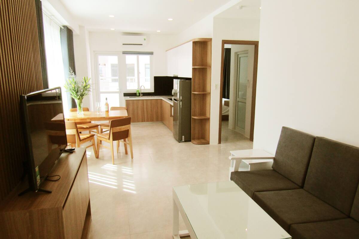 A modern living room with a glass coffee table, a brown sofa, and a dining area with wooden chairs and a table.
