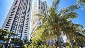 A tall building with a modern architectural design, surrounded by palm trees and greenery. - SoHo Apartment (Bac Nha Trang)