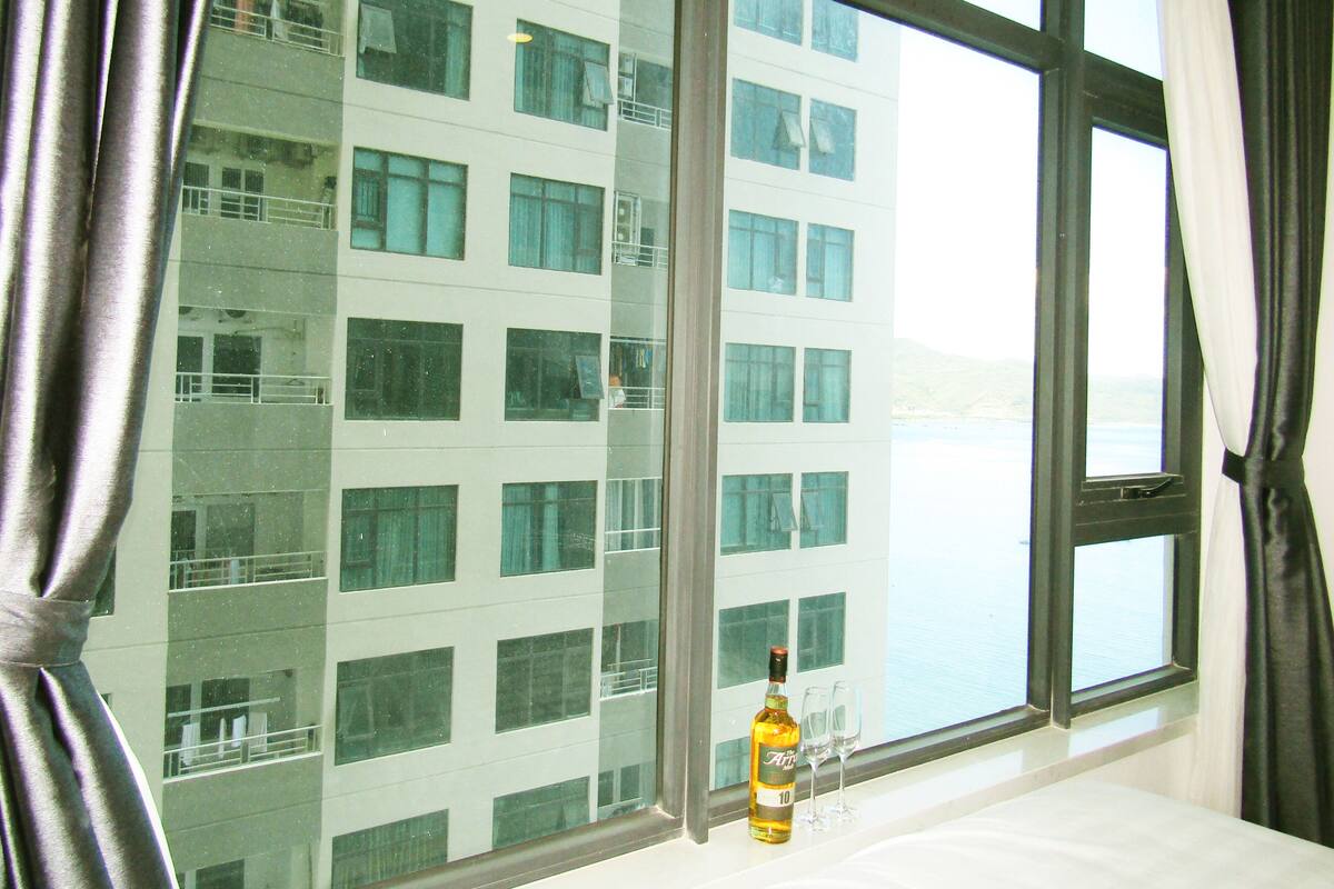 A bottle of alcohol and two glasses on a windowsill, with a view of a building through the window.