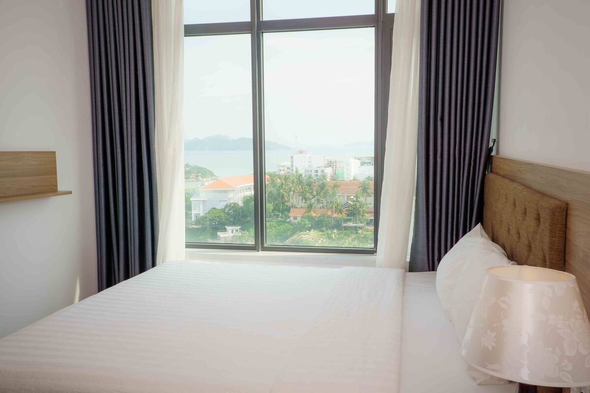 A hotel room with a large window, a bed, and a nightstand with a lamp.