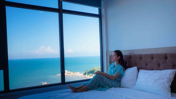 A bed with a view of the ocean through large windows. - SoHo Apartment (Bac Nha Trang)