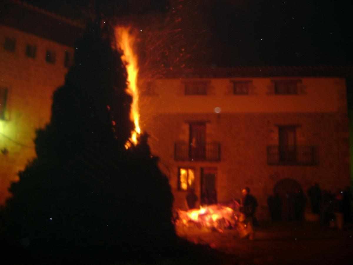 Un edificio con varias ventanas y balcones, un fuego ardiendo al frente y algunas personas en el fondo.