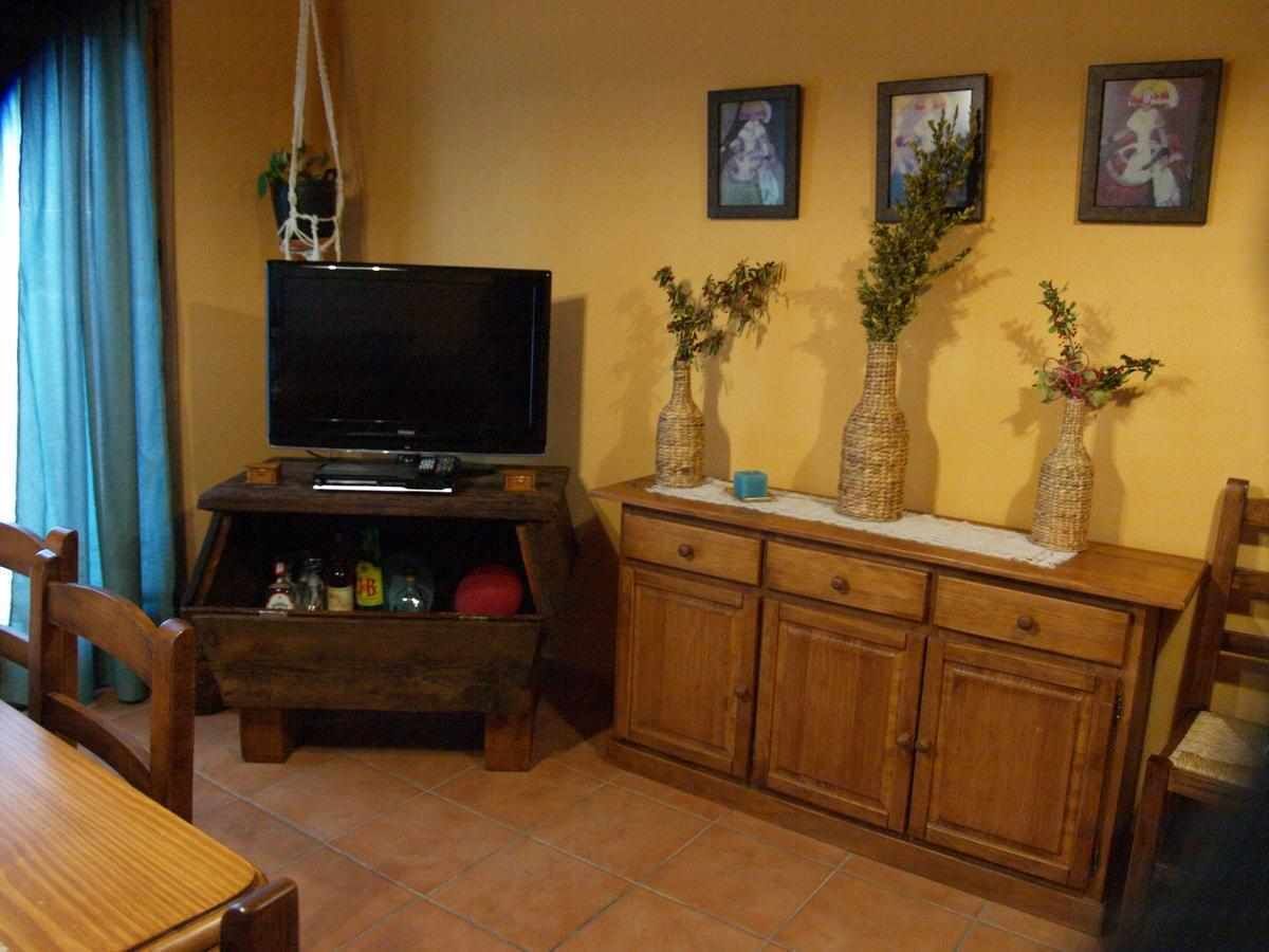 Una sala de estar con televisor, armarios de madera y tres jarrones en un estante.