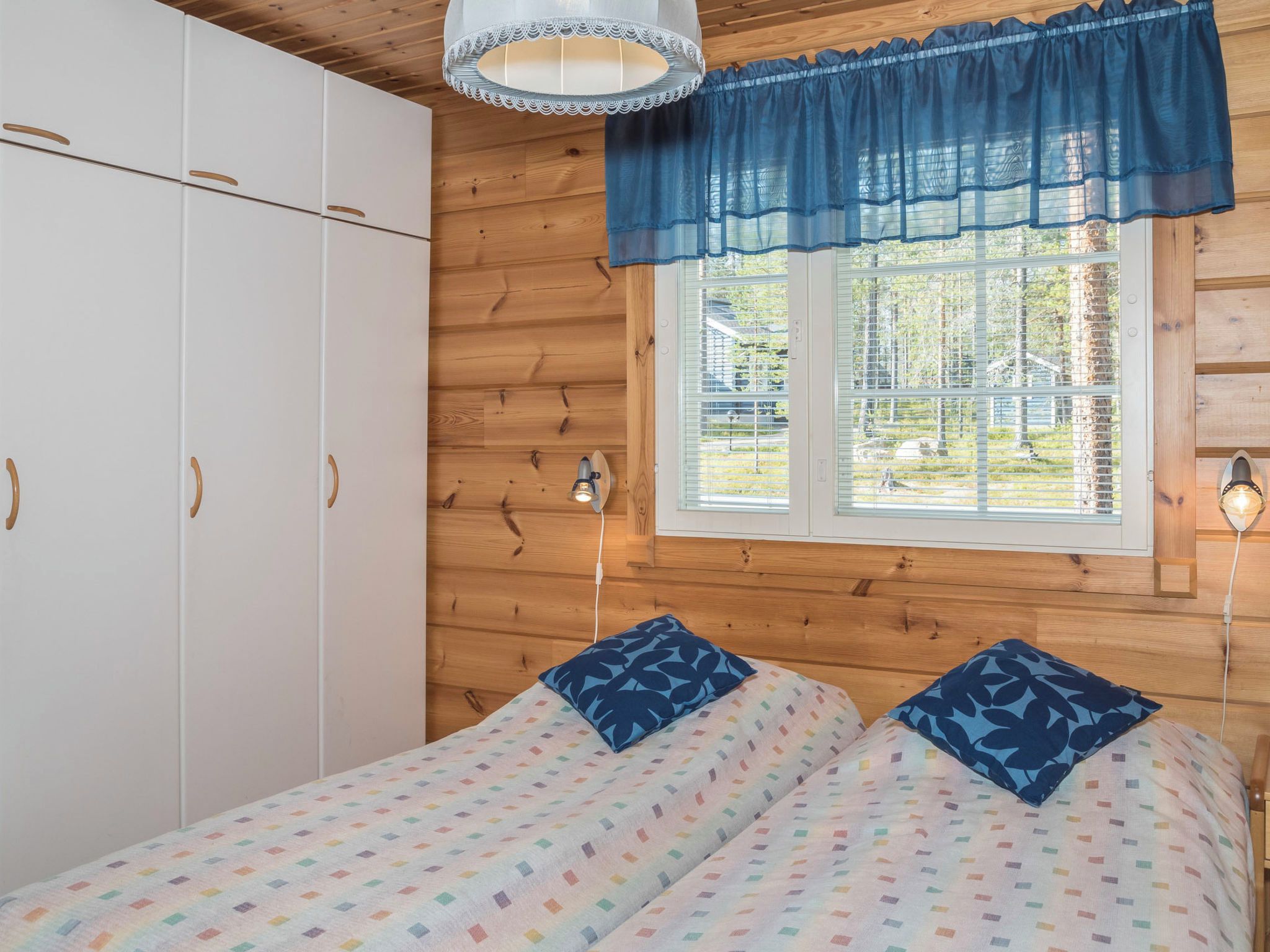 A bedroom with a bed, a wardrobe, a window with blinds, and a wall-mounted lamp.