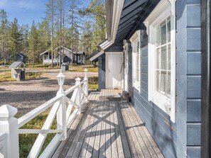 A wooden deck leading to a house with a white door and windows, surrounded by a fence and trees.
