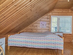 A bedroom with a sloped ceiling, a bed with a colorful quilt, a nightstand, a chair, and a window with blinds. - Koskelo by Interhome (Äkäslompolo)