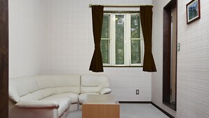 Een kamer met een witte hoekbank, een houten salontafel, een raam met gordijnen, en een schilderij aan de muur.
