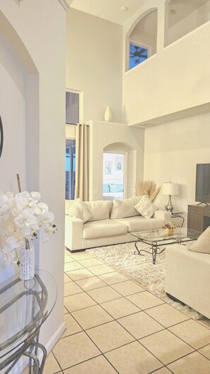 A spacious living area with a high ceiling, a glass coffee table, a sofa, and a TV.