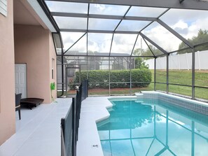 A covered outdoor swimming pool with a glass enclosure, a door, and a small seating area.